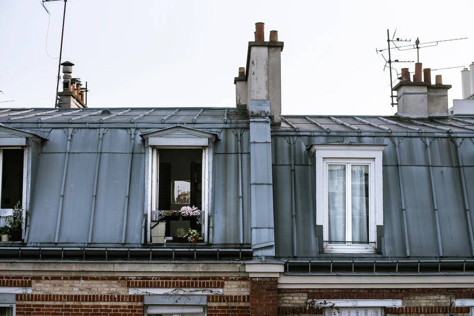 Ouvrier en combinaison de protection intégrale blanche travaillant sur toiture en ardoises, utilisant une échelle aluminium pour accéder aux tuiles défaillantes